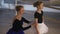 Side view of concentrated slim gorgeous woman adjusting white tutu of cute Caucasian girl standing at barre in dance