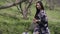 Side view of confident beautiful Asian young woman in kimono sitting on green spring meadow in park touching long black