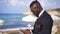 Side view of confident happy African American handsome man in suit with boutonniere texting on smartphone admiring