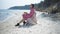 Side view confident intelligent beautiful woman sitting on sandy beach with book looking away. Wide shot Caucasian