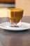 Side view of Cortado coffee in a small glass with ceramic saucer on metallic table