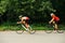 Side view of a couple riding bikes on a road through park with overgrown trees