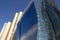 Side view of a curved blue glass window wall of a modern and elegant corporative building, next to a yellowish classical one.