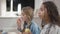 Side view of cute Caucasian girl enjoying healthful apple in classroom with blurred African American classmate eating