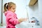 Side view of cute little girl with ponytail in pink bathrobe washing her hands.