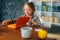 Side view of cute pupil school girl kid doing homework reading paper book sitting at table in light children room.