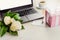 Side view of a deck with computer, bouquet of peonies flowers, cup of coffee, empty card and pink dotted gift box. White rustic wo