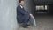 Side view of desperate businessman sitting down leaned against the wall in urban underground crossing. Depressed