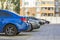 Side view detail of cars row parked in paved yard parking lot area on blurred building background on bright sunny day.