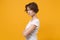 Side view of displeased young brunette woman in white t-shirt posing isolated on yellow orange background in studio