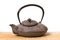 Side view of eastern iron teapot with a half opened lid on wooden mat