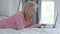 Side view of engrossed Caucasian businesswoman lying on bed and using laptop. Absorbed mid-adult woman in eyeglasses