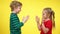 Side view of excited carefree boy and girl playing hand clapping game at yellow background. Happy Caucasian brother and