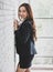 Side view of excited ethnic female entrepreneur in classy jacket leaning on wall in modern office and smiling  with happy, fun