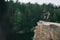 side view of extreme trial bikers standing on back wheels on rocky cliff with blurred pine forest