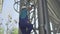 Side view of factory worker climbing up the ladder on enormous stainless steel cement storage silo. Camera follows