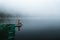 Side view of fashioned young woman sitting on wooden dock looking at view on a misty morning