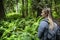 Side view of Female Hiker walking through a lush wooded forest in the beautiful Pacific Northwest full of ferns and mossy trees.