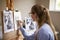 Side View Of Female Teenage Artist Sitting At Easel Drawing Picture Of Dog From Photograph In Charcoal