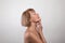 Side view of feminine nude senior woman touching silky skin on her neck, light studio background. Aged beauty concept