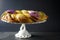 Side view of a festive Mardi Gras King Cake with green, gold, and purple frosting on a white cake stand with a gray background