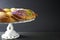 Side view of a festive Mardi Gras King Cake with green, gold, and purple frosting on a white cake stand with a gray background;