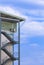 Side view of fire escape with rain gutter system and air conditioning compressor on industrial building wall against white clouds