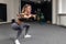 Side view of fitness woman with blond and pink long hair doing full length squats exercise with gymnastic stick, blurred