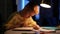 Side view of focused cute little student boy reading paper book following lines with finger along page sitting at table