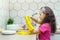 Side view of focused preteen girl with long dark hair wearing pink T-shirt, putting on yellow gloves, looking at hands.