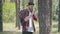 Side view of focused young bearded environmentalist examining tree in summer forest. Portrait of concentrated handsome