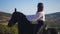 Side view of gorgeous confident equestrian in sunglasses sitting on purebred black stallion admiring beauty of nature in