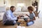 Side view of grandad and granddaughter sitting opposite each other cross legged on the floor in the living room constructing a mod