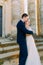 The side view of the groom hugging the bride back while standing on the stair of the ancient castle.