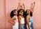 Side view of a group of young women raising hands up. Three females wearing headphones while standing against a pink wall