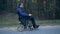 Side view of a handicapped man moving along the road in his powered wheelchair
