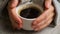 Side view of hands with cup of black coffe on light wooden table background. White cup of black coffee.