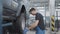 Side view of handsome brunette Caucasian auto mechanic examining car wheel in auto repair shop. Portrait of confident