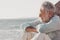 Side view of handsome senior man, white haired, sitting on the beach looking at horizon over water