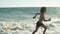 Side view of happy Caucasian little boy running along coastline