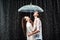 side view of happy couple in white shirts standing under umbrella under raindrops