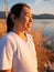 Side view of happy hopeful woman looking away to nature reflection on water at sunset lakeside