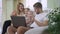 Side view of happy smiling Caucasian young man waving at laptop with blurred daughters and wife at background. Positive