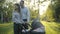 Side view of happy smiling couple of parents standing at sunset in park with baby stroller. Positive Caucasian man and