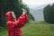 Side view of a hiker woman taking selfie on her mobile phone, wearing a red raincoat in the pouring rain in the mountain forest.