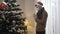 Side view of hopeful young man in Covid-19 face mask praying to Christmas tree at home. Portrait of Caucasian guy asking