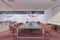 Side view on huge grey conference table and red chairs on red carpet in light meeting room with glass walls and city view from big