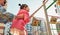 Side view image of active cute little girl climbing on a rope at playground. Mother helping her daughter to climb on a wall with a