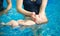 Side view of infant floating on back. Cropped snapshot of female mother`s hands holding her baby during swimming lesson