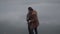 Side view of laughing Caucasian couple hugging at the background of grey water on cloudy day. Positive young man and